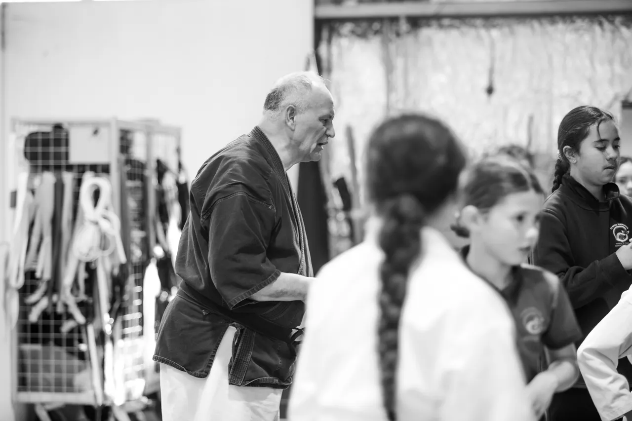The kaiako moves down the line in his black gi as students turn to follow him